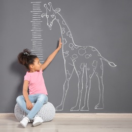 African-American child near grey wall with chalk giraffe drawing and height meter