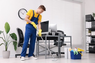 Photo of Cleaning service worker washing floor with mop and bucket of supplies in office