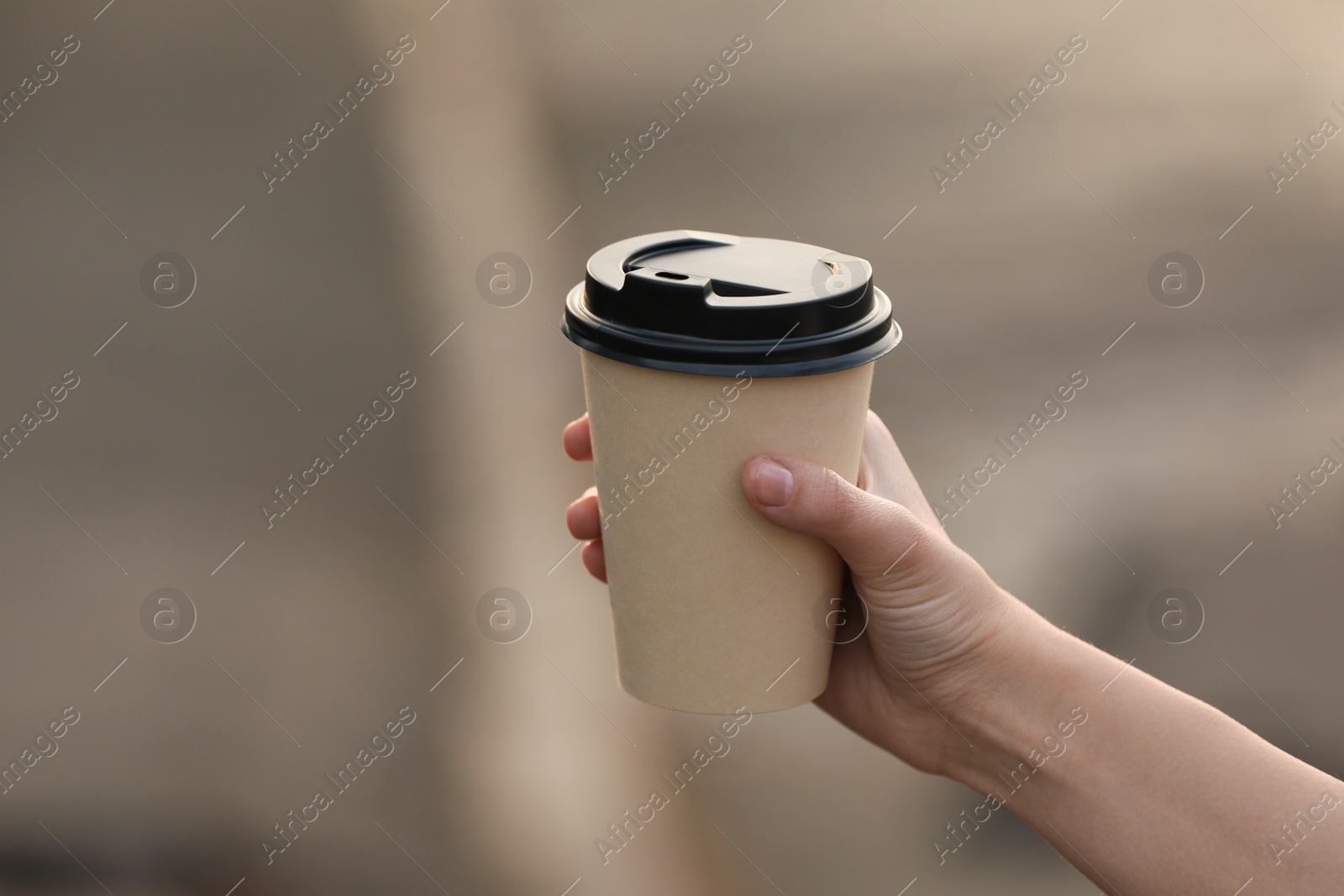 Photo of Woman holding paper coffee cup on blurred background, closeup