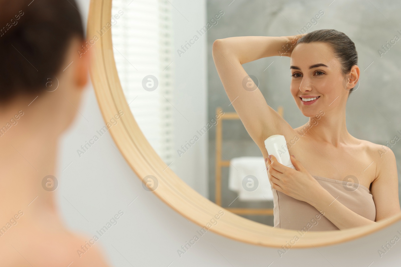 Photo of Beautiful woman applying deodorant near mirror in bathroom