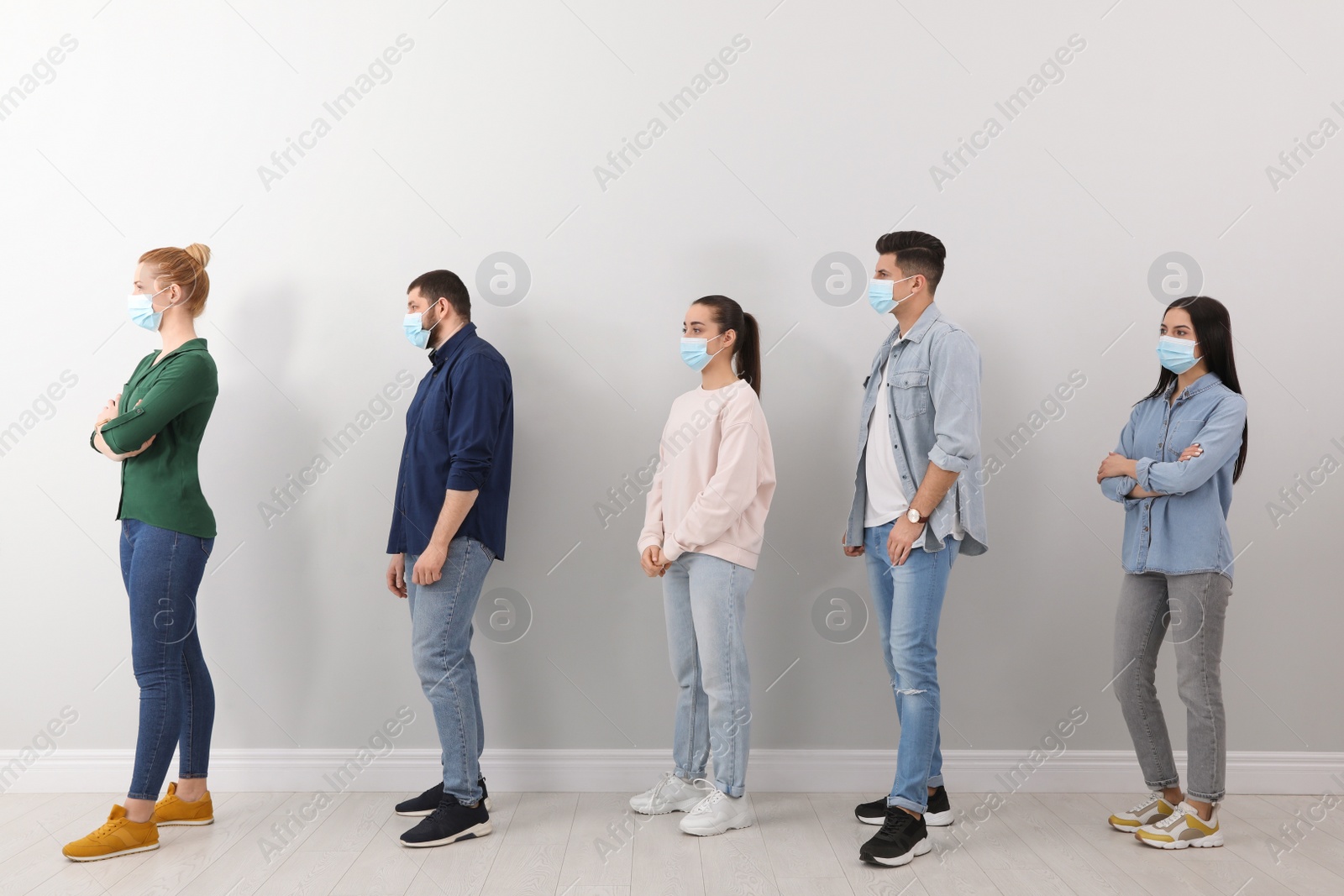 Photo of People with protective masks waiting in queue near light wall indoors. Social distancing during Covid-19 pandemic