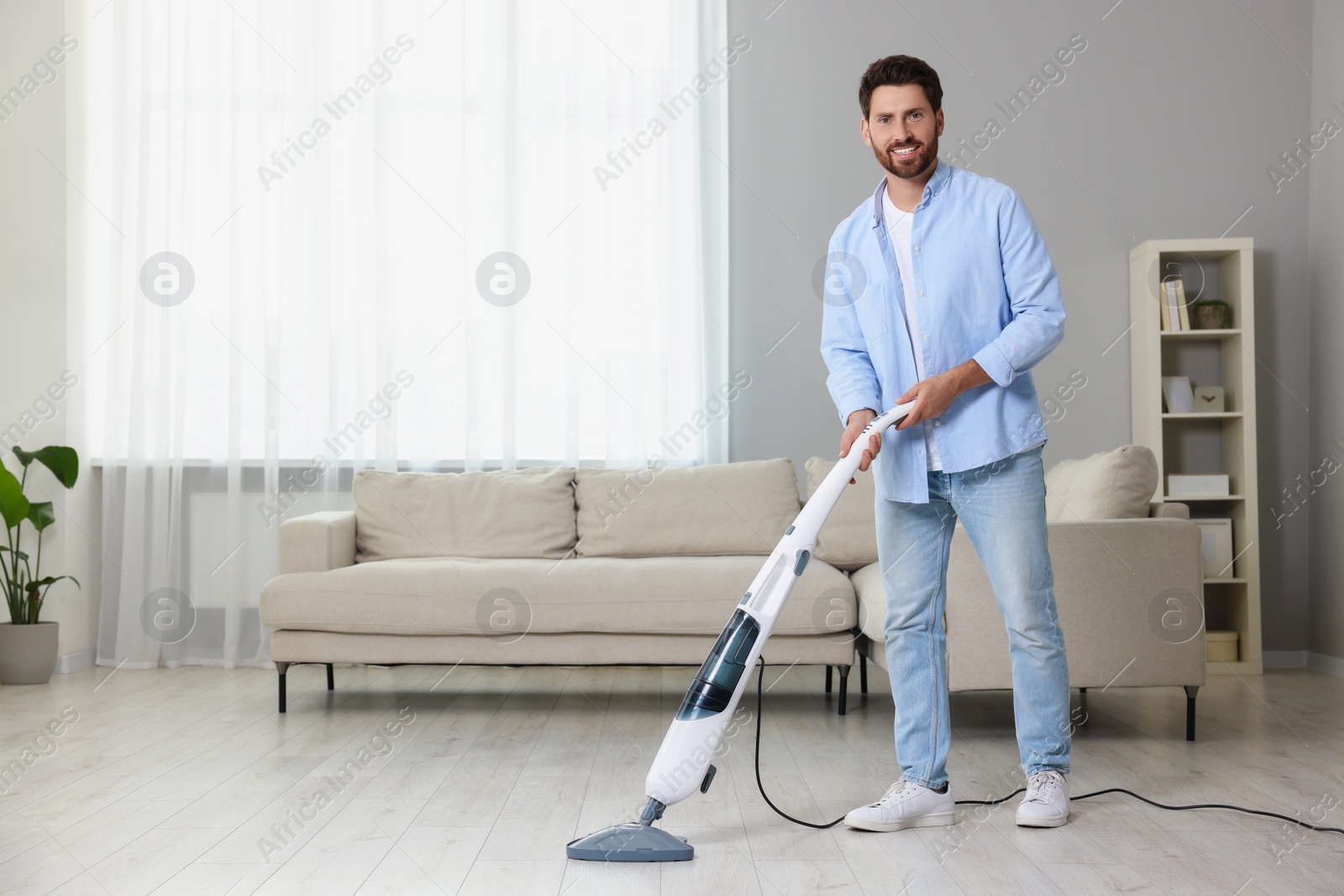 Photo of Happy man cleaning floor with steam mop at home. Space for text