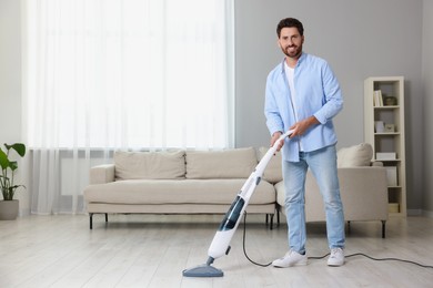 Happy man cleaning floor with steam mop at home. Space for text