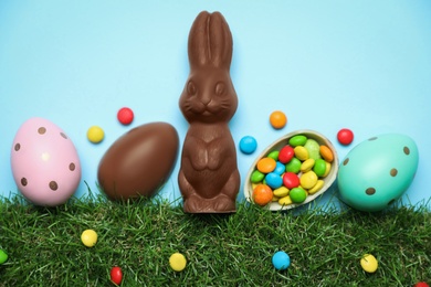 Photo of Chocolate Easter bunny, eggs and candies with green grass on light blue background