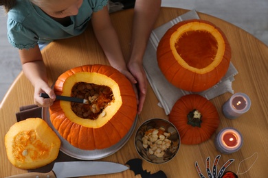 Photo of Mother and daughter making pumpkin jack o'lantern at wooden table, top view. Halloween celebration