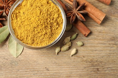 Photo of Curry powder in bowl and other spices on wooden table, flat lay. Space for text