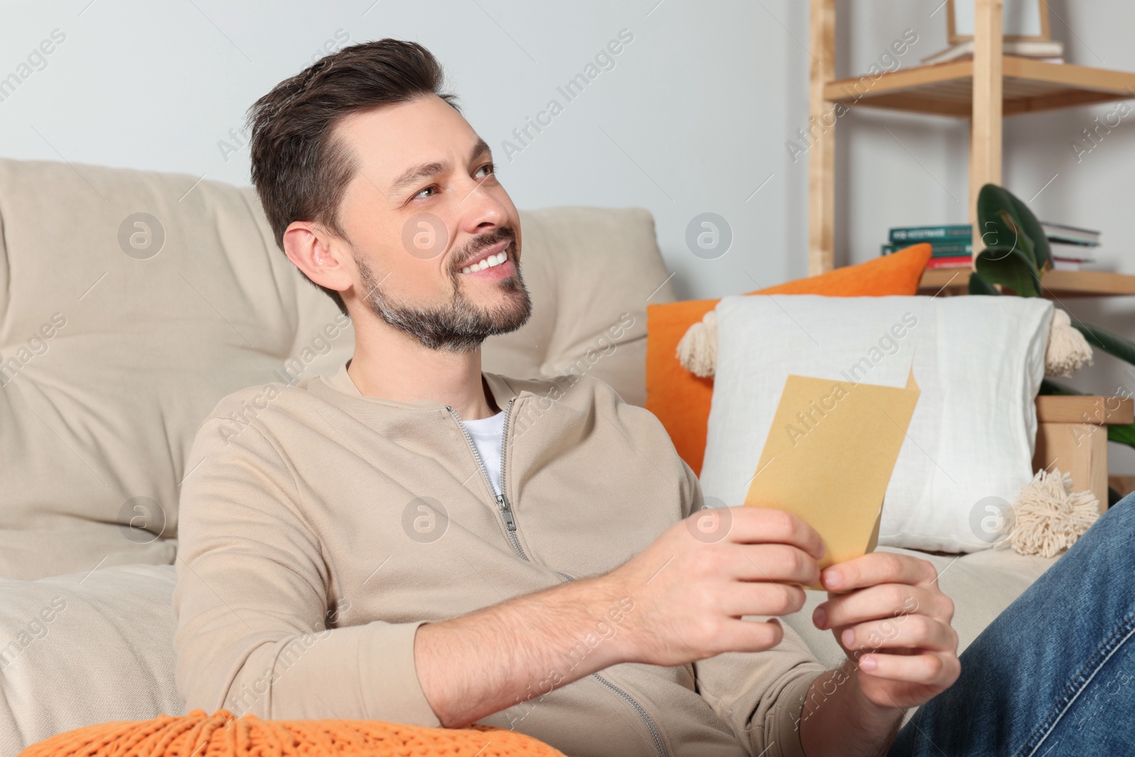 Photo of Happy man holding greeting card on sofa in living room