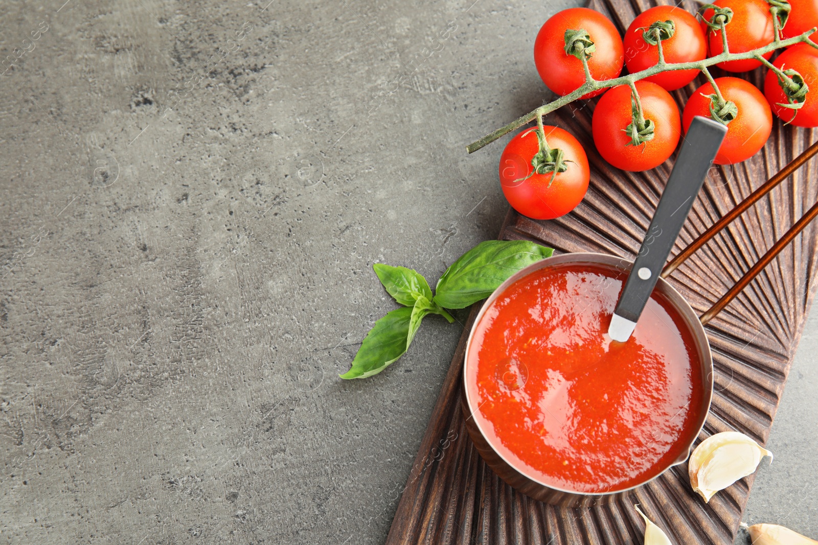 Photo of Flat lay composition with pan of sauce and tomatoes on grey table. Space for text