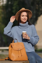 Photo of Young woman with stylish backpack and hot drink on autumn day