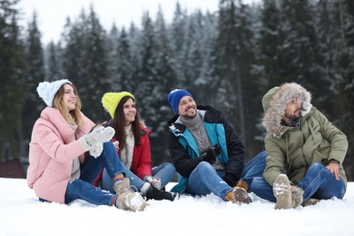 Photo of Group of friends sitting on snow outdoors. Winter vacation