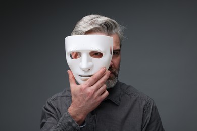 Photo of Multiple personality concept. Man covering face with mask on dark grey background