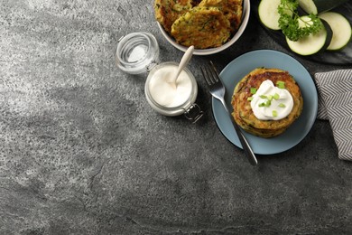 Photo of Delicious zucchini pancakes with sour cream served on grey table, flat lay. Space for text