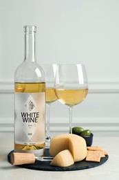Photo of Bottle of white wine, glasses and crackers with cheese on table