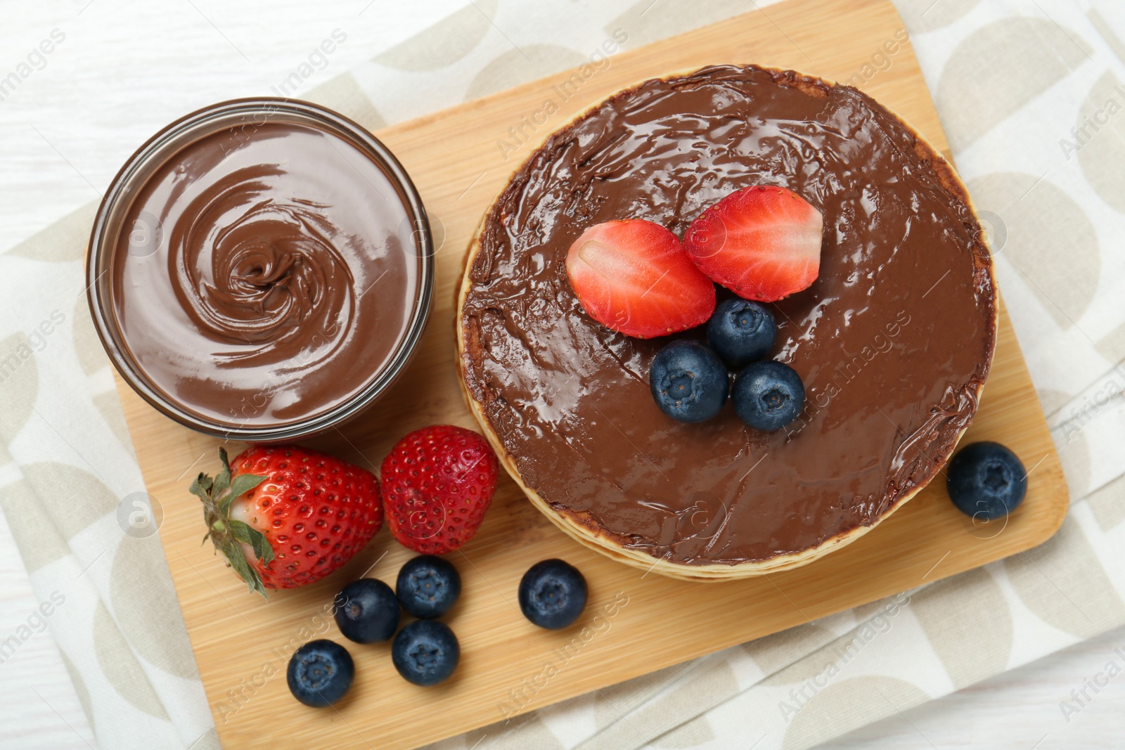 Photo of Tasty pancakes with chocolate paste and berries on white wooden table, top view