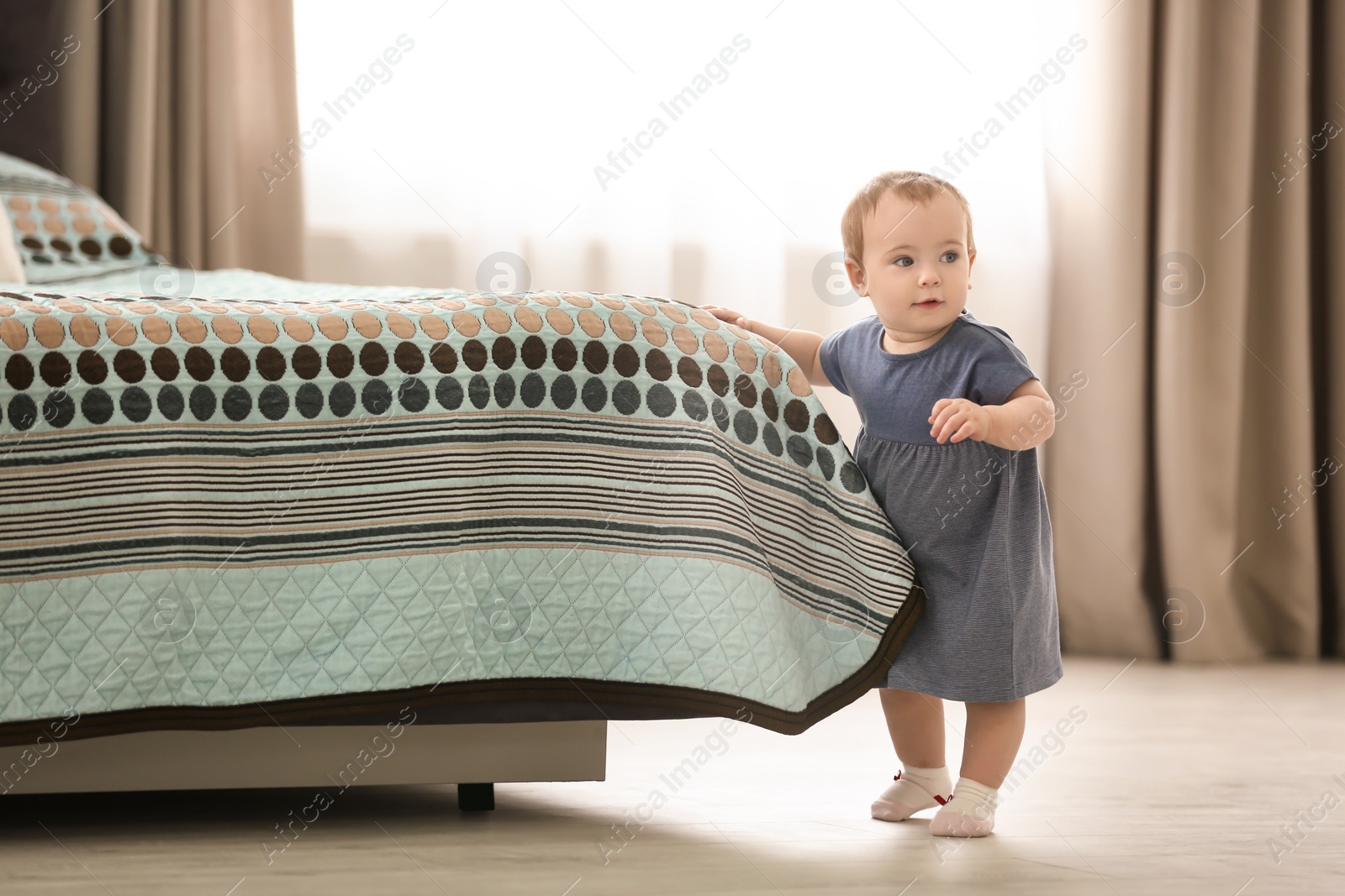 Photo of Cute baby holding on to bed at home. Learning to walk