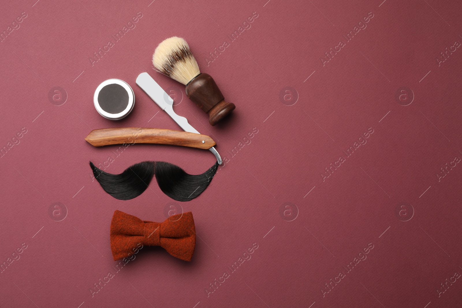 Photo of Artificial moustache and barber tools on burgundy background, flat lay. Space for text