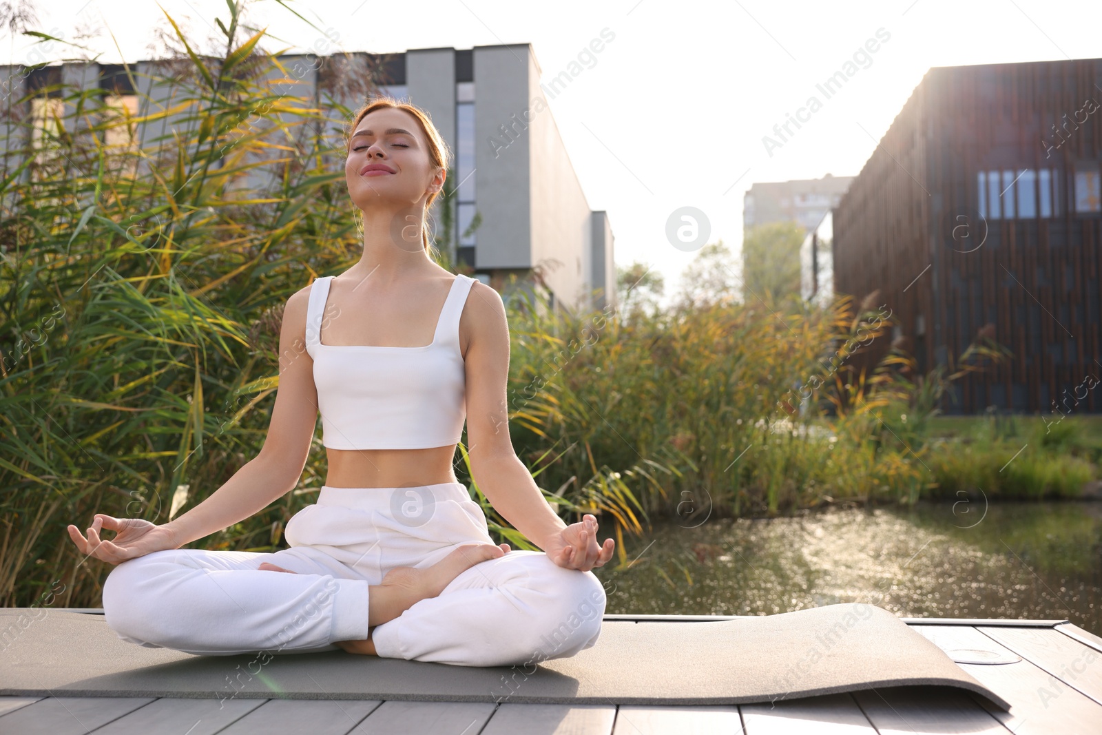 Photo of Beautiful young woman practicing Padmasana on yoga mat outdoors. Lotus pose