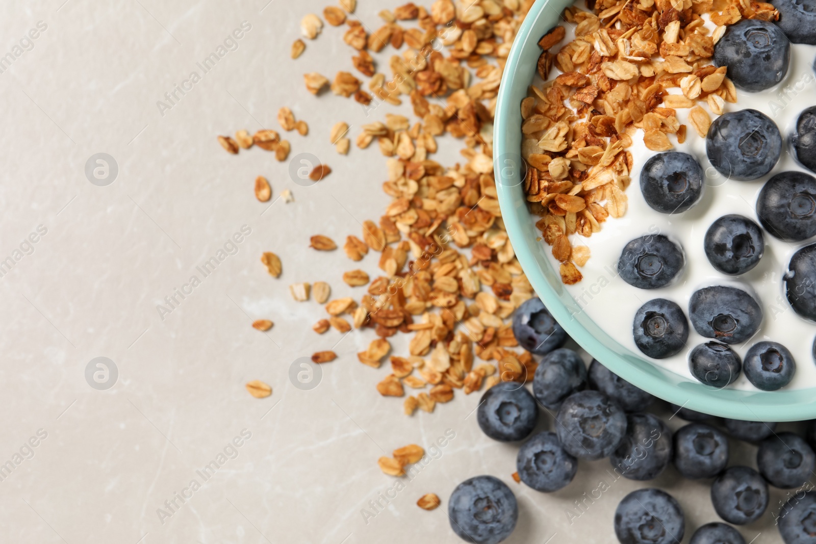 Photo of Bowl of yogurt with granola and blueberries on grey marble table, flat lay. Space for text