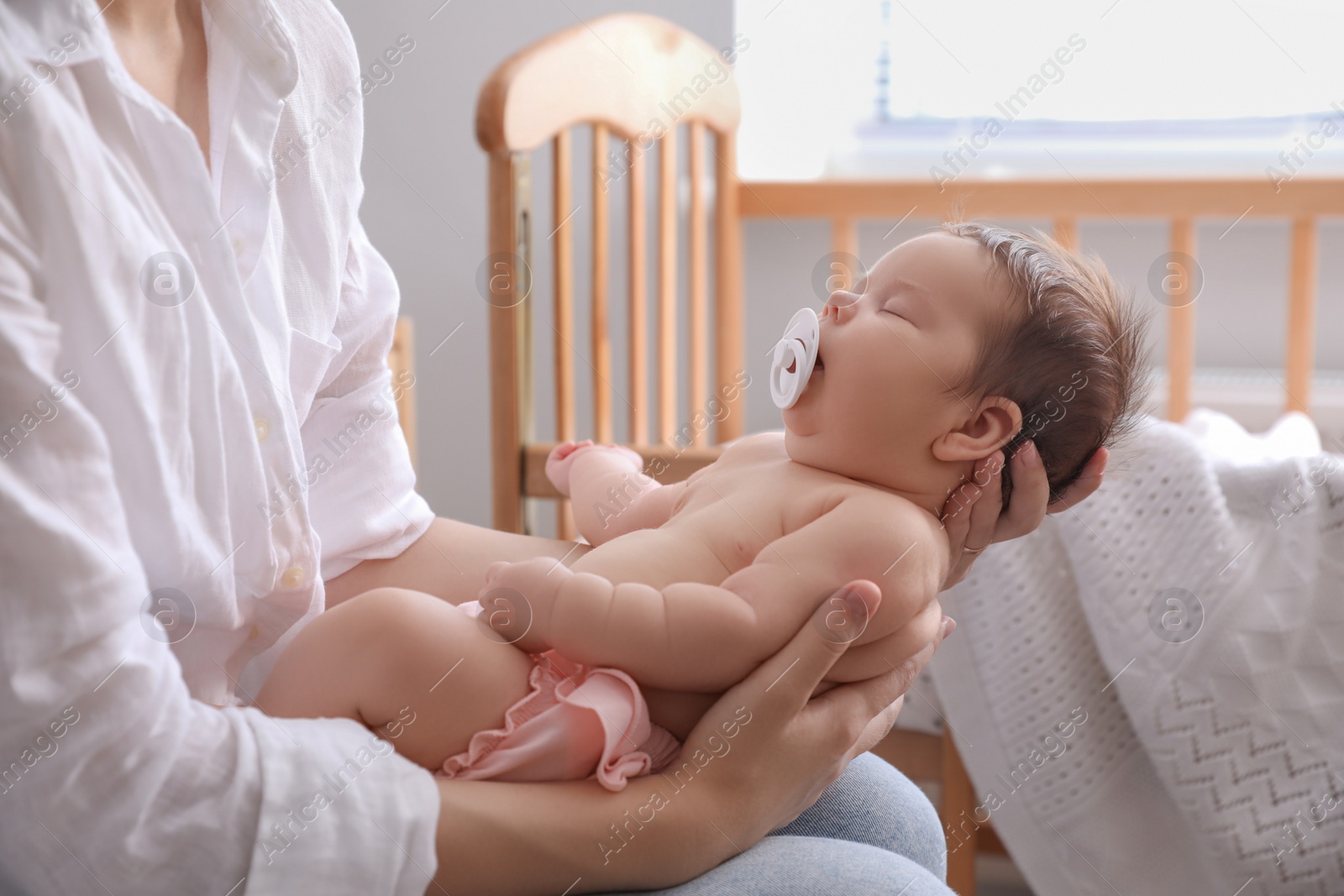 Photo of Mother holding her cute little baby with pacifier at home, closeup