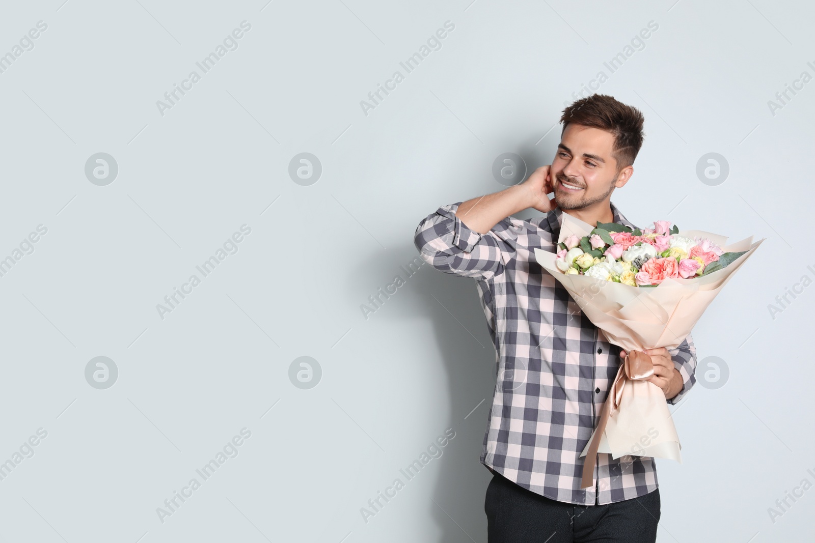 Photo of Young handsome man with beautiful flower bouquet on light background, space for text