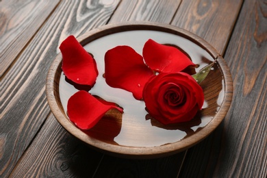 Bowl with aroma spa water, rose and petals on wooden background