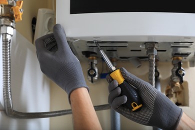 Photo of Man repairing gas boiler with screwdriver indoors, closeup