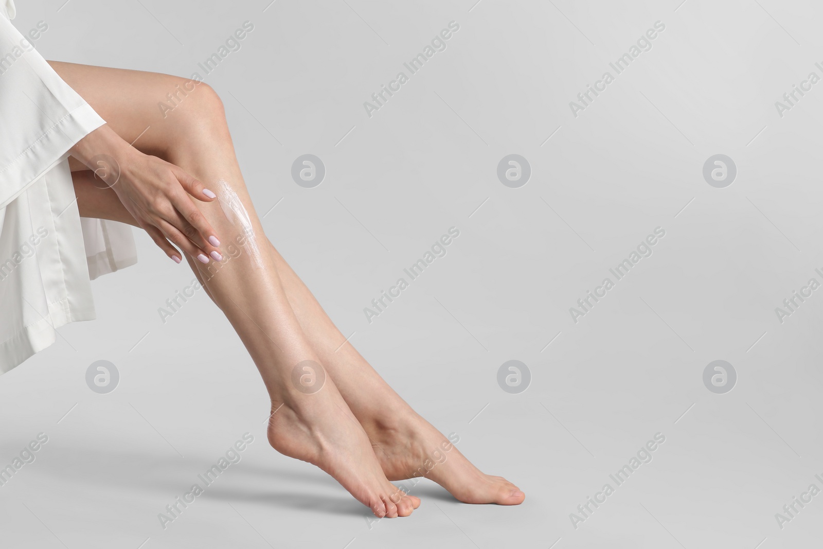 Photo of Woman applying body cream onto her smooth legs on light grey background, closeup. Space for text