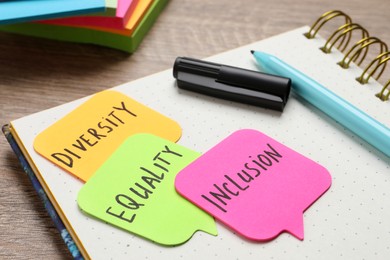 Photo of Sticky notes with words Diversity, Equality, Inclusion and stationery on wooden table, closeup
