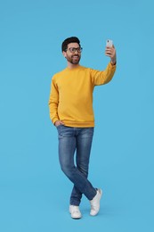 Photo of Smiling man taking selfie with smartphone on light blue background