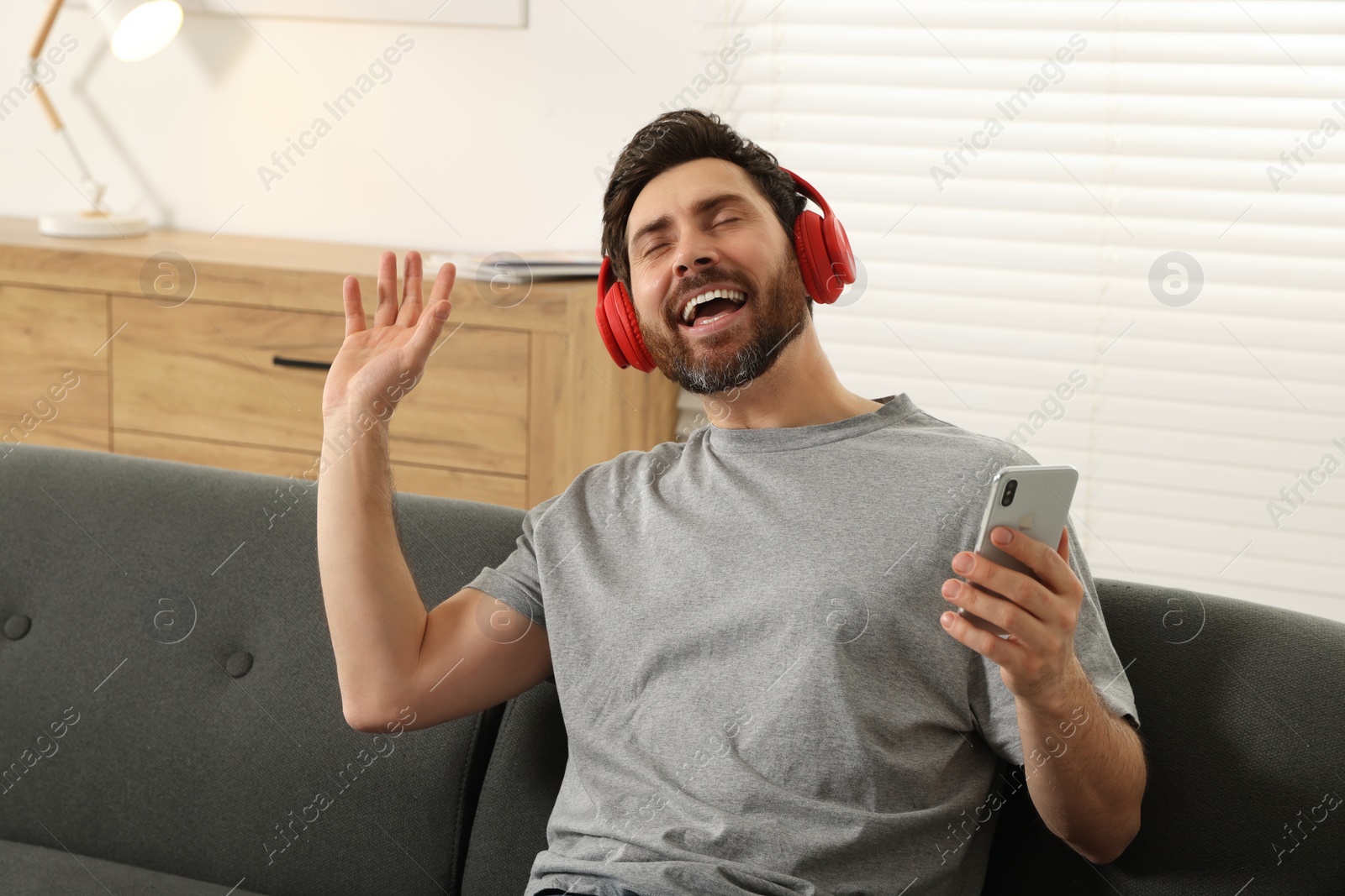 Photo of Happy man listening music with headphones on sofa indoors