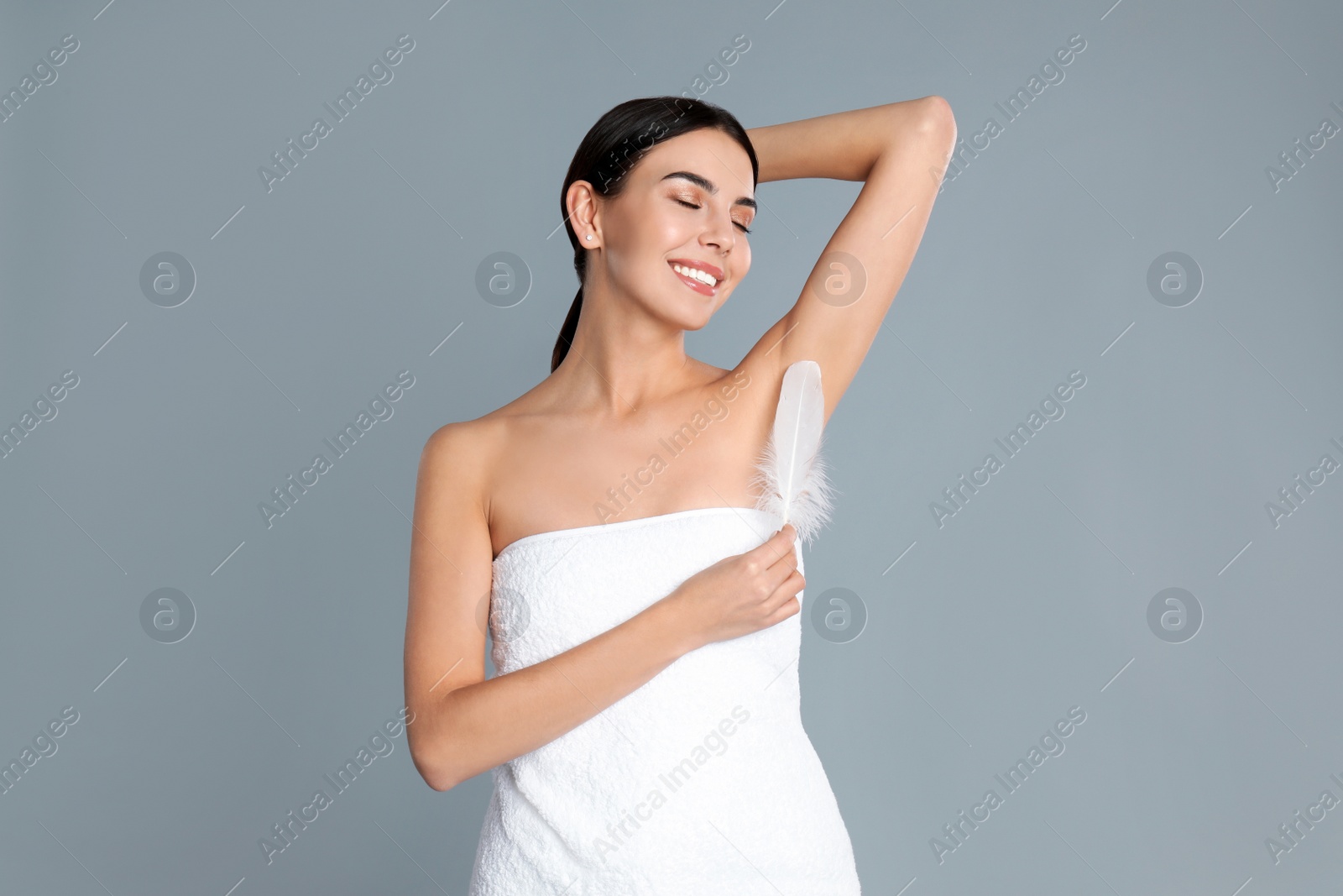 Photo of Young woman touching armpit with feather after epilation procedure on grey background