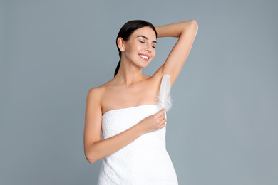 Young woman touching armpit with feather after epilation procedure on grey background