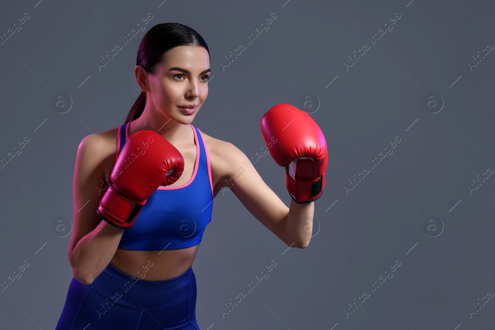 Photo of Beautiful woman wearing boxing gloves training in color lights on grey background. Space for text
