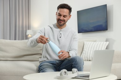 Photo of Man opening light blue thermo bottle indoors