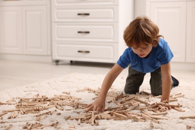 Cute little boy playing with wooden construction set on carpet at home, space for text. Child's toy