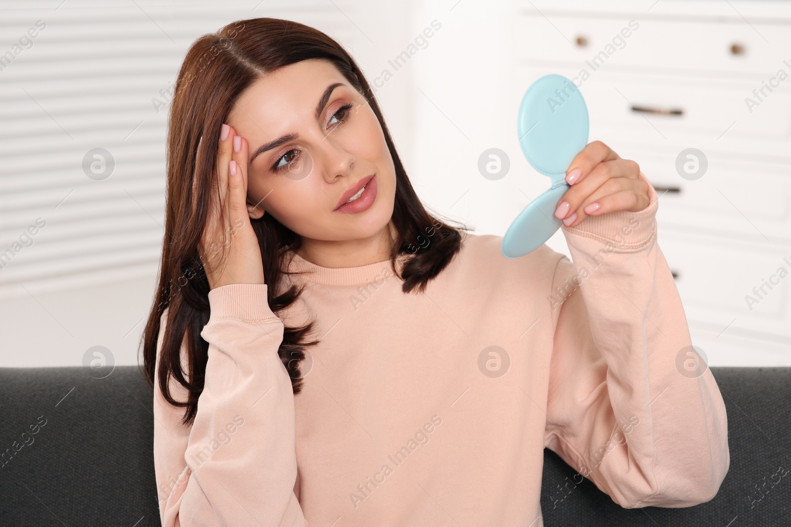 Photo of Young woman looking in mirror and touching her face indoors. Hormonal disorders