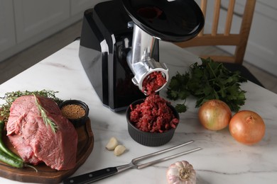 Electric meat grinder with beef mince and products on white marble table in kitchen