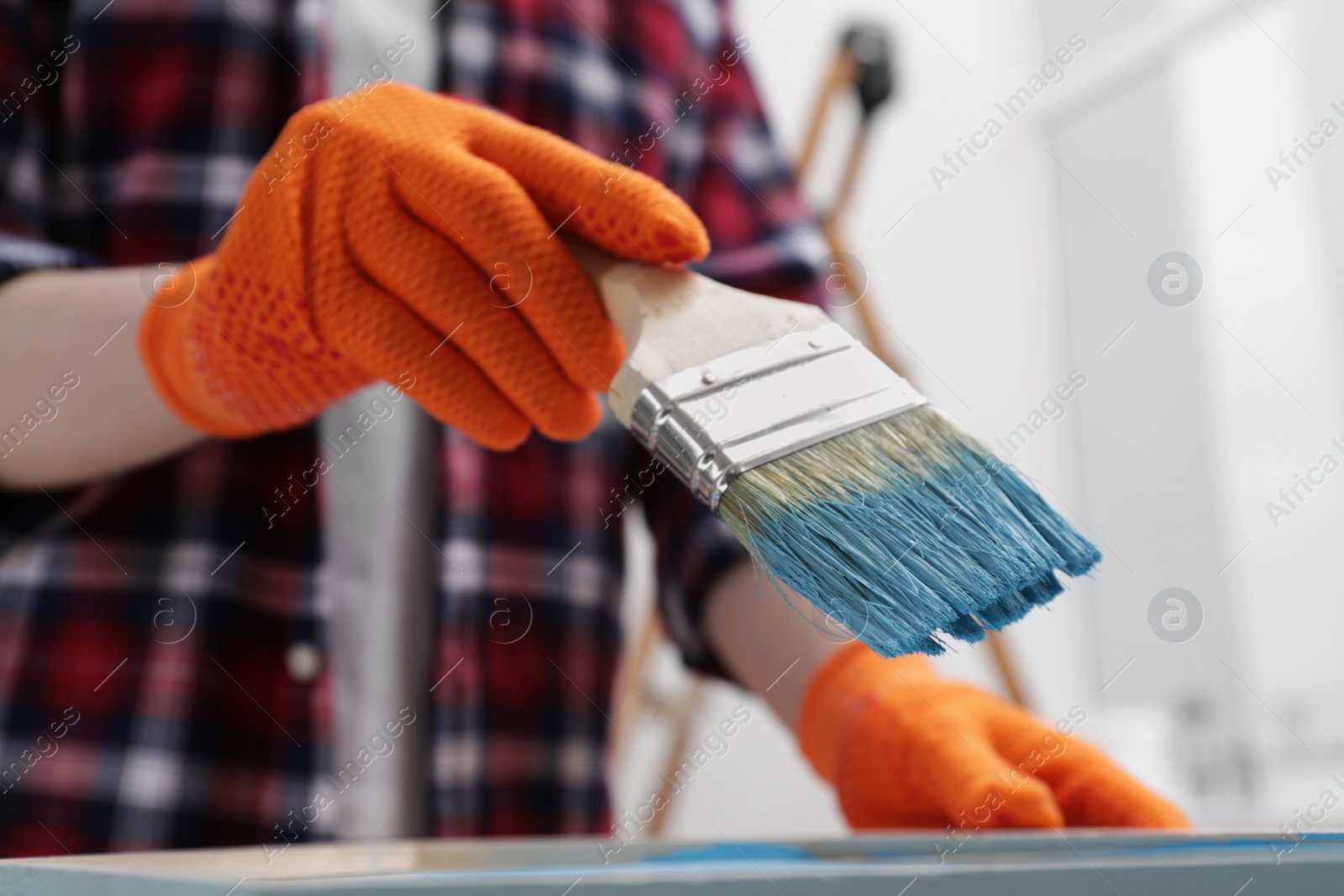 Photo of Woman holding brush with light blue paint indoors, closeup