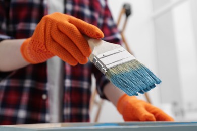 Woman holding brush with light blue paint indoors, closeup