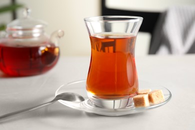 Traditional Turkish tea in glass and sugar cubes on white table, closeup