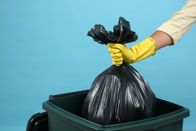 Photo of Woman throwing garbage bag into bin on light blue background, closeup