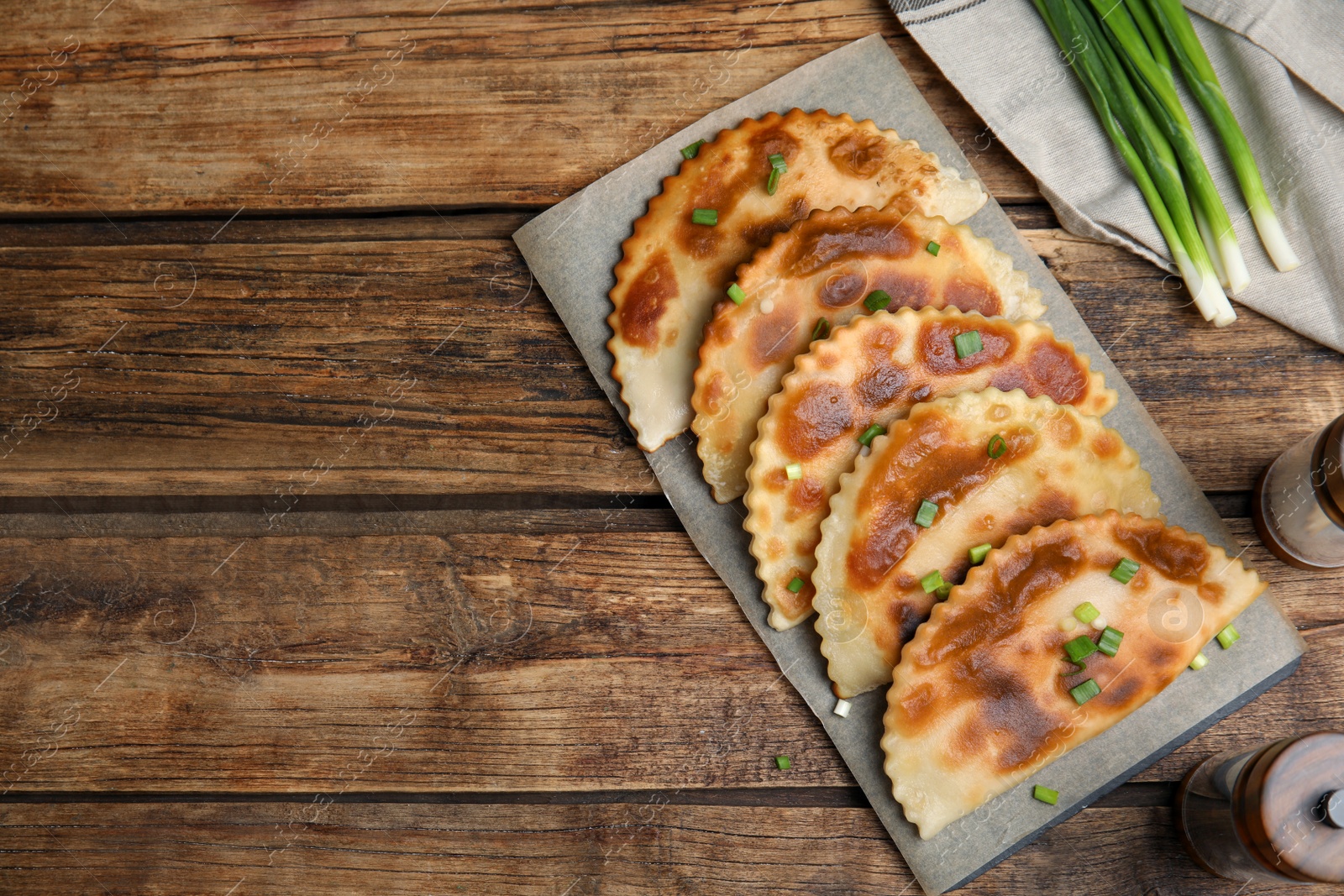 Photo of Board with delicious fried chebureki and onion on wooden table, flat lay. Space for text