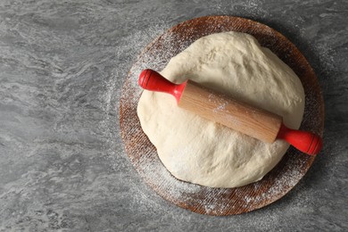 Photo of Raw dough and rolling pin on grey table, top view. Space for text