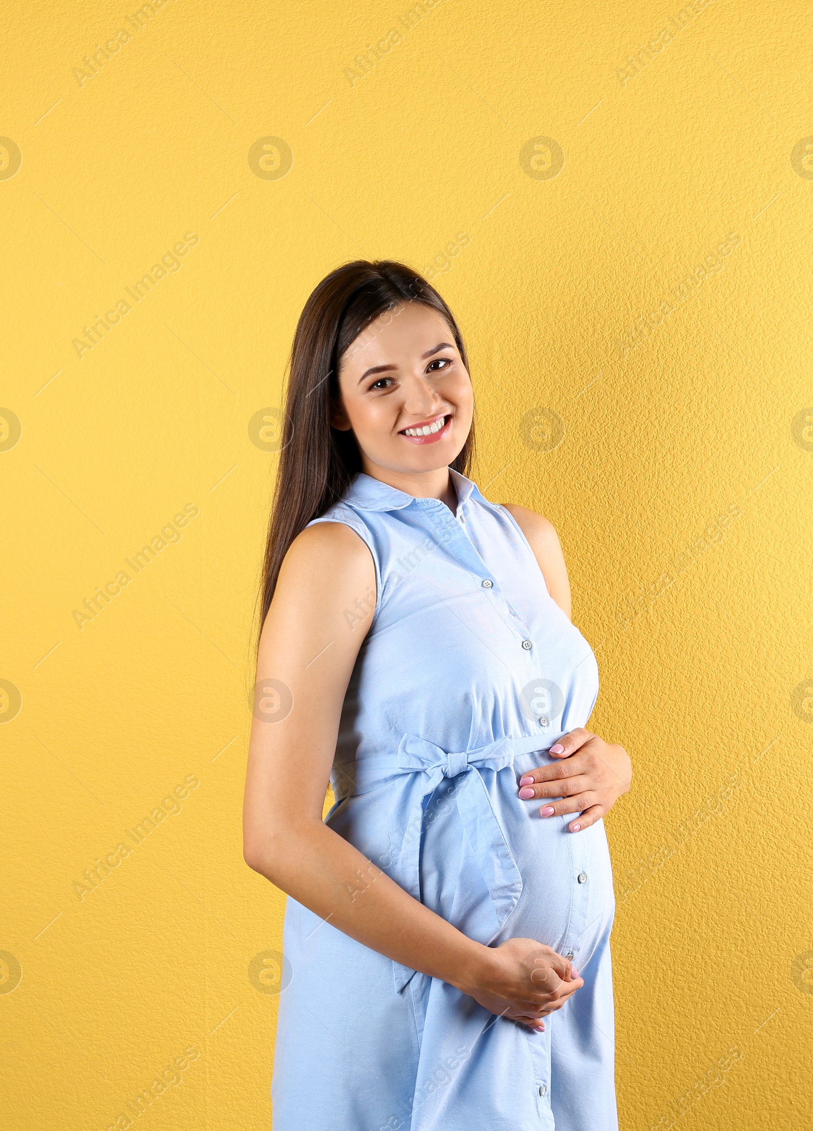 Photo of Beautiful pregnant woman holding hands on belly against color background