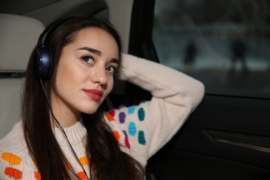 Beautiful young woman listening to music with headphones in car. Space for text