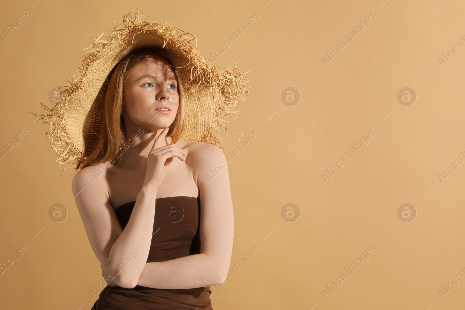 Photo of Beautiful young woman in straw hat on beige background, space for text