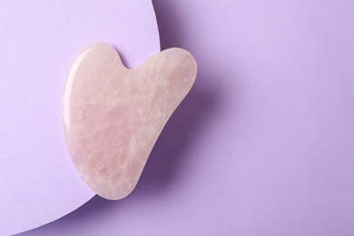 Photo of Rose quartz gua sha tool on violet background, top view. Space for text