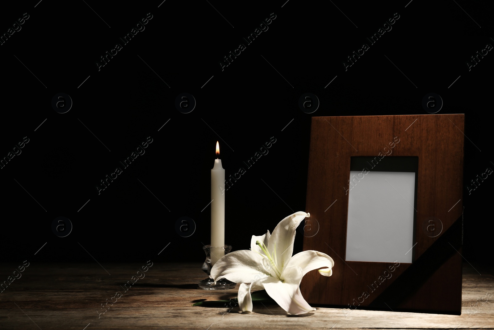 Photo of Funeral photo frame, burning candle and white lily on dark background