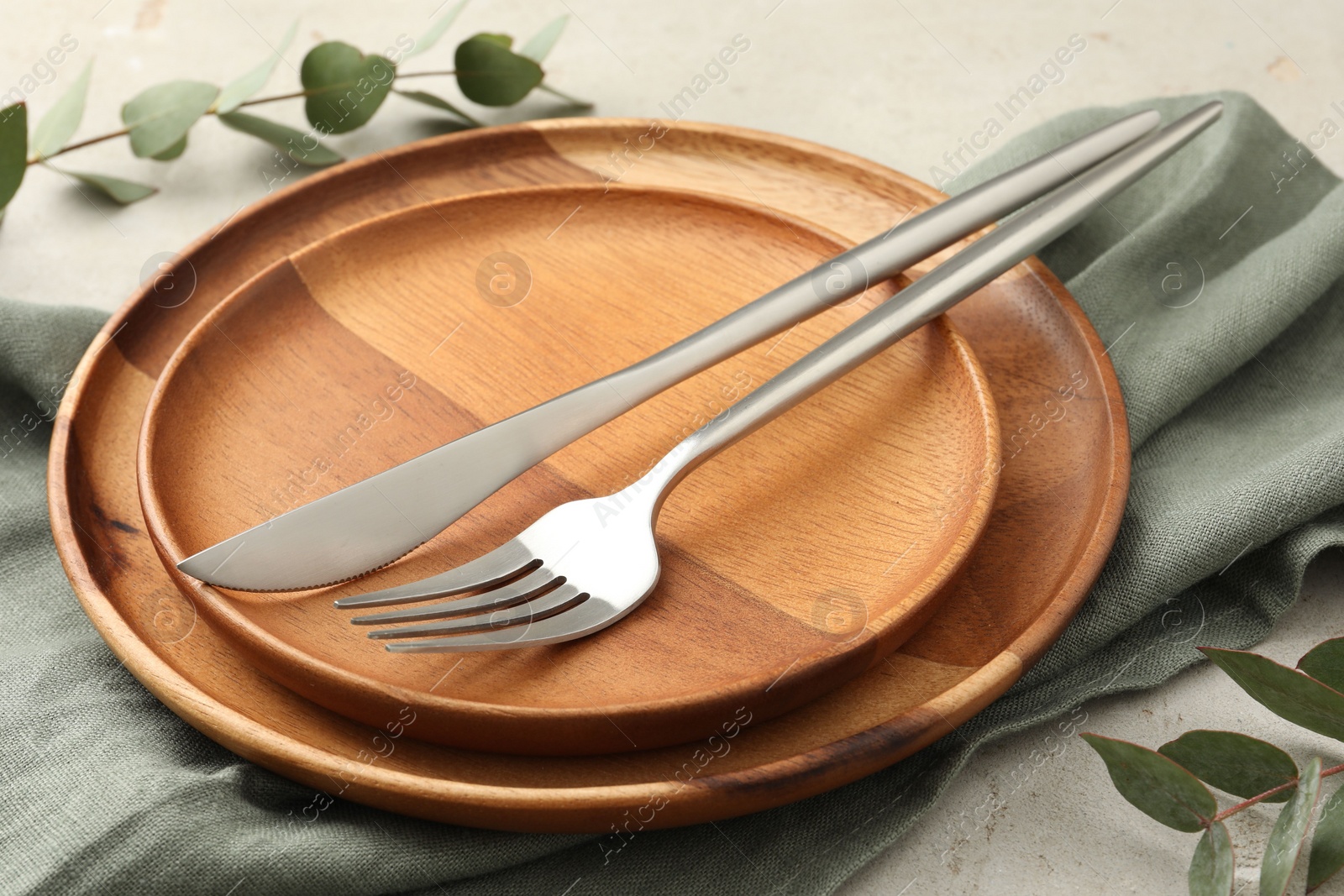 Photo of Stylish setting with cutlery, napkin, eucalyptus branches and plates on light table, closeup