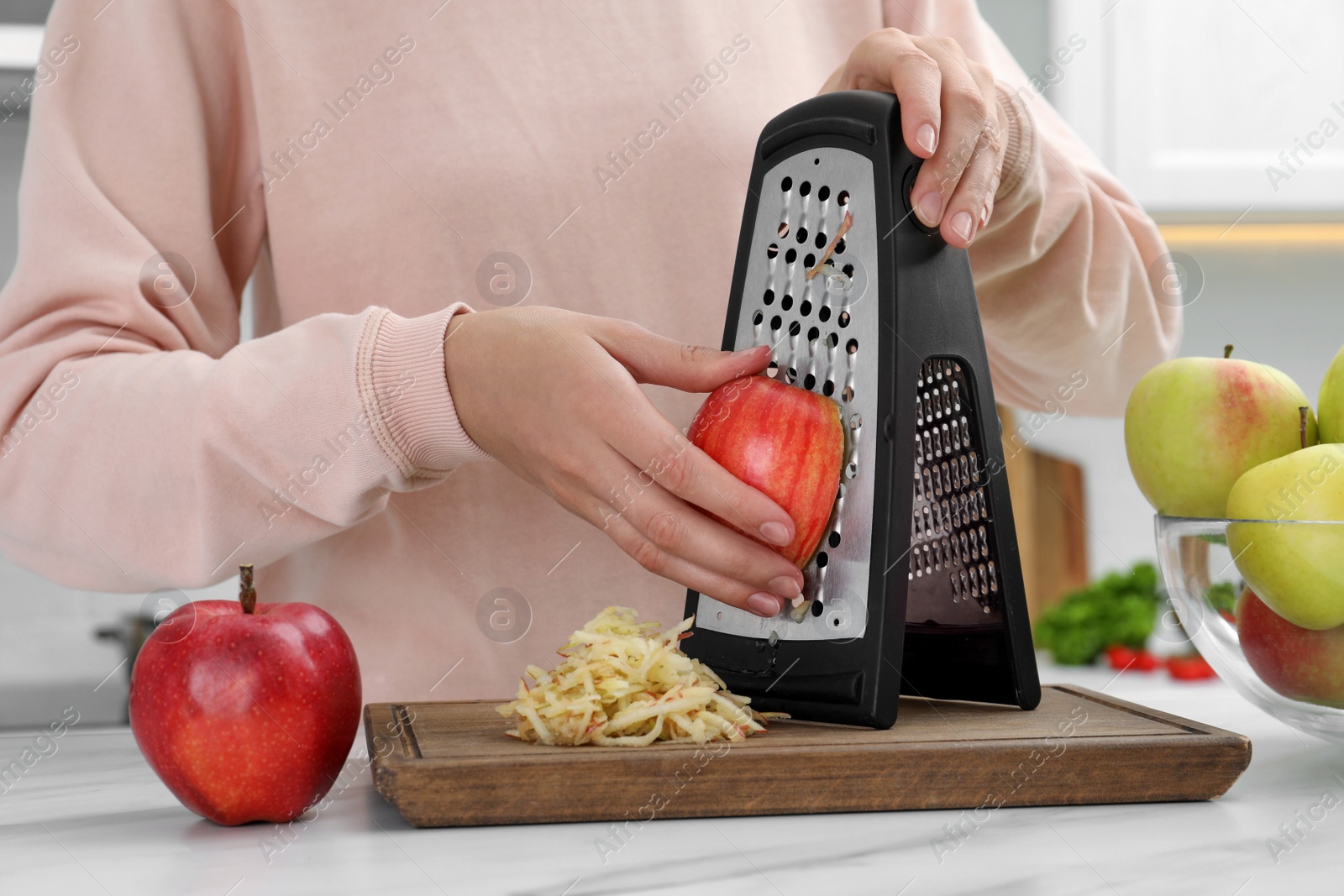 Photo of Woman grating fresh red apple at kitchen table, closeup